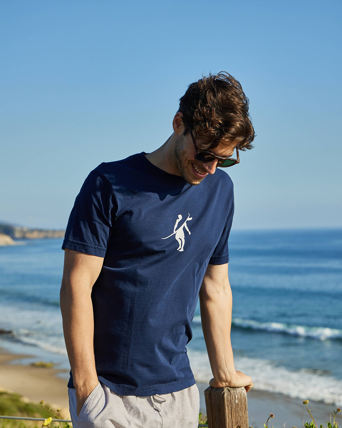 Men's navy t-shirt with Toes on the Nose logo, worn at the beach, with a scenic ocean view.