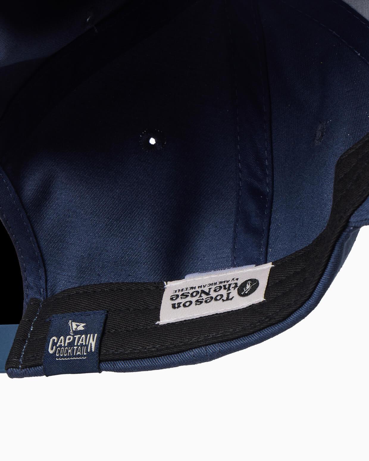 Navy blue cap with visible brand labels Toes on the Nose and Captain Cocktail on a white background