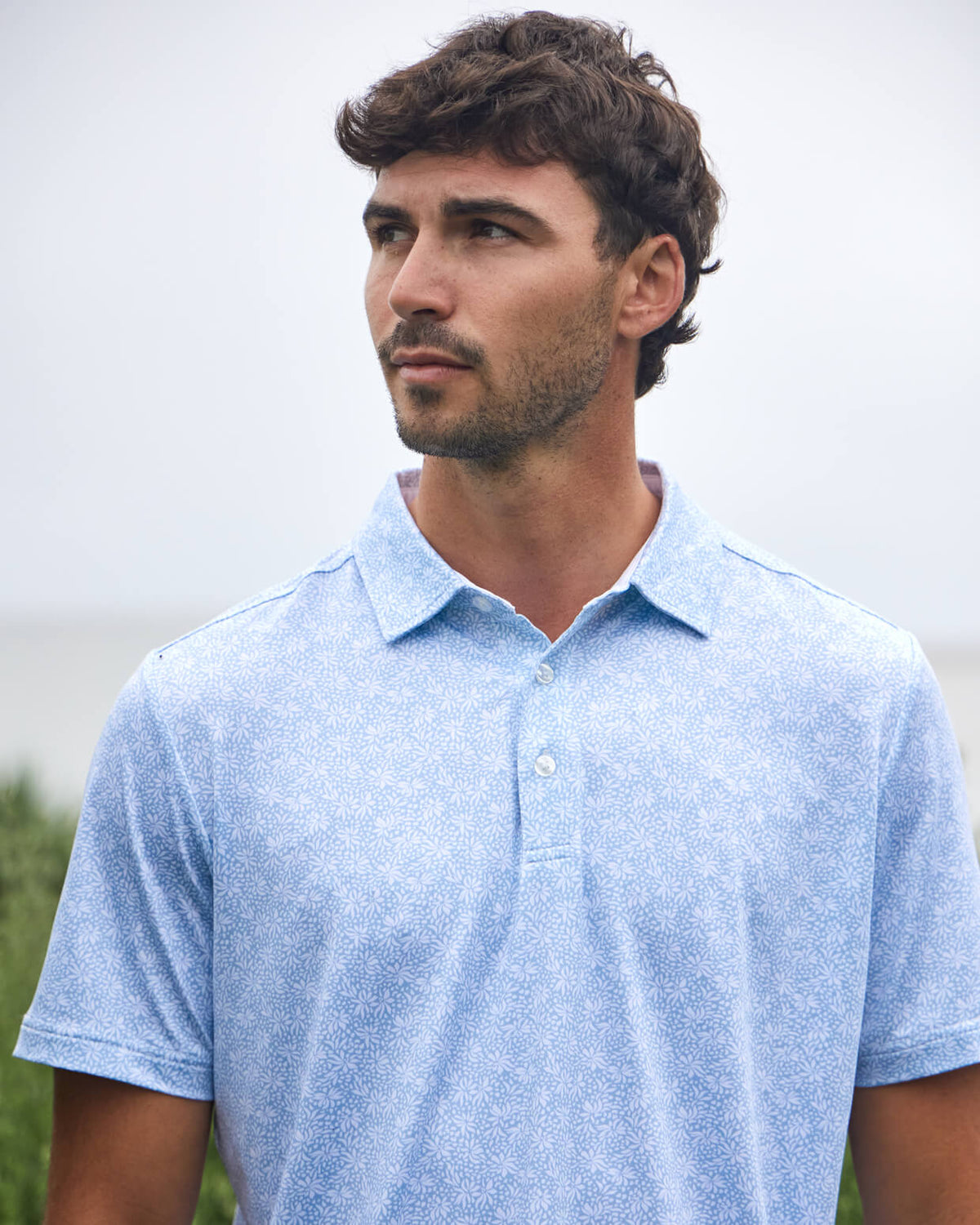 Men's sky blue floral polo from Toes on the Nose, worn in a lifestyle setting outdoors. #color_sky blue floral