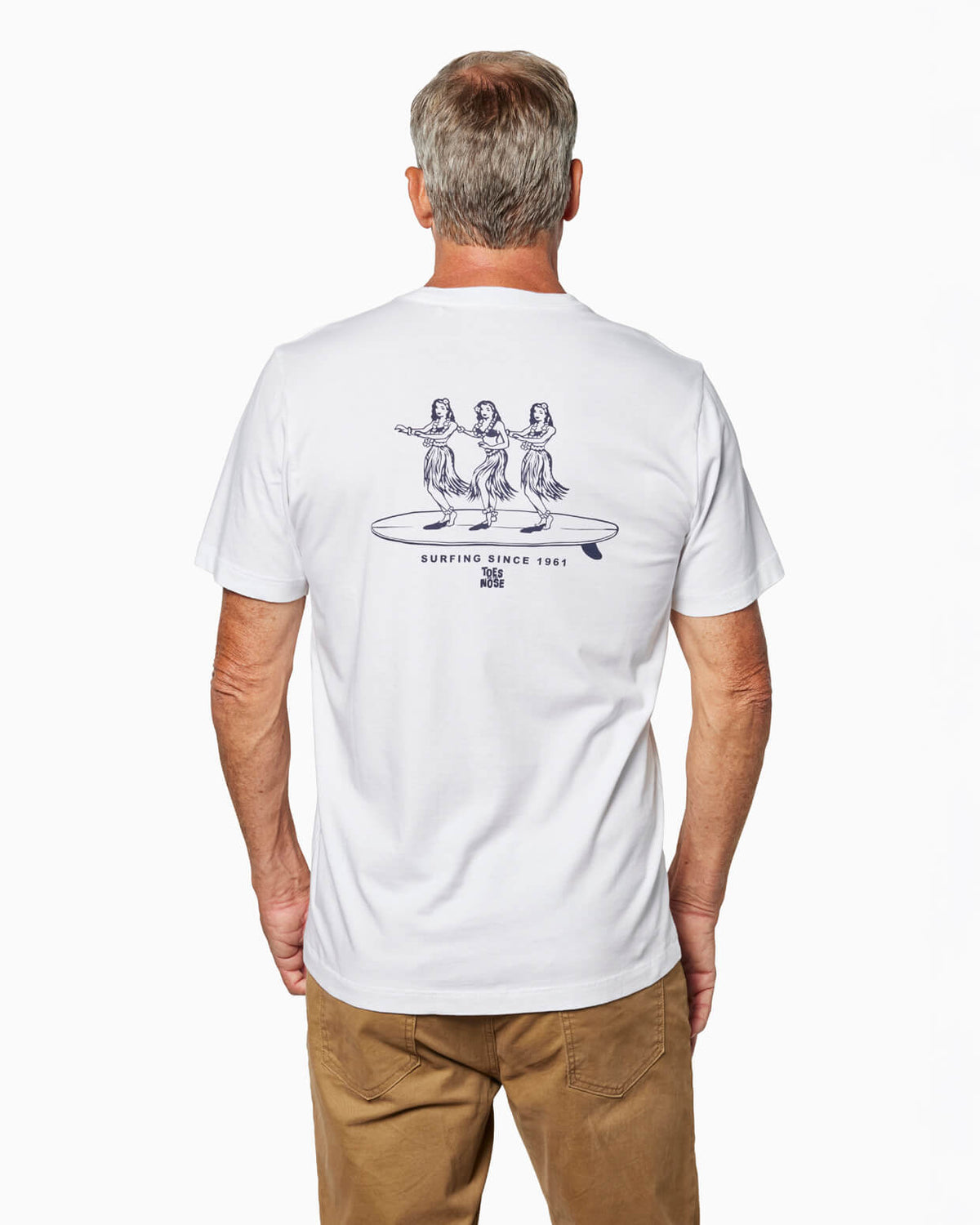 Man wearing a white t-shirt Toes on the Nose hula girls on surfboard graphic design on the back, standing against a white background #color_white