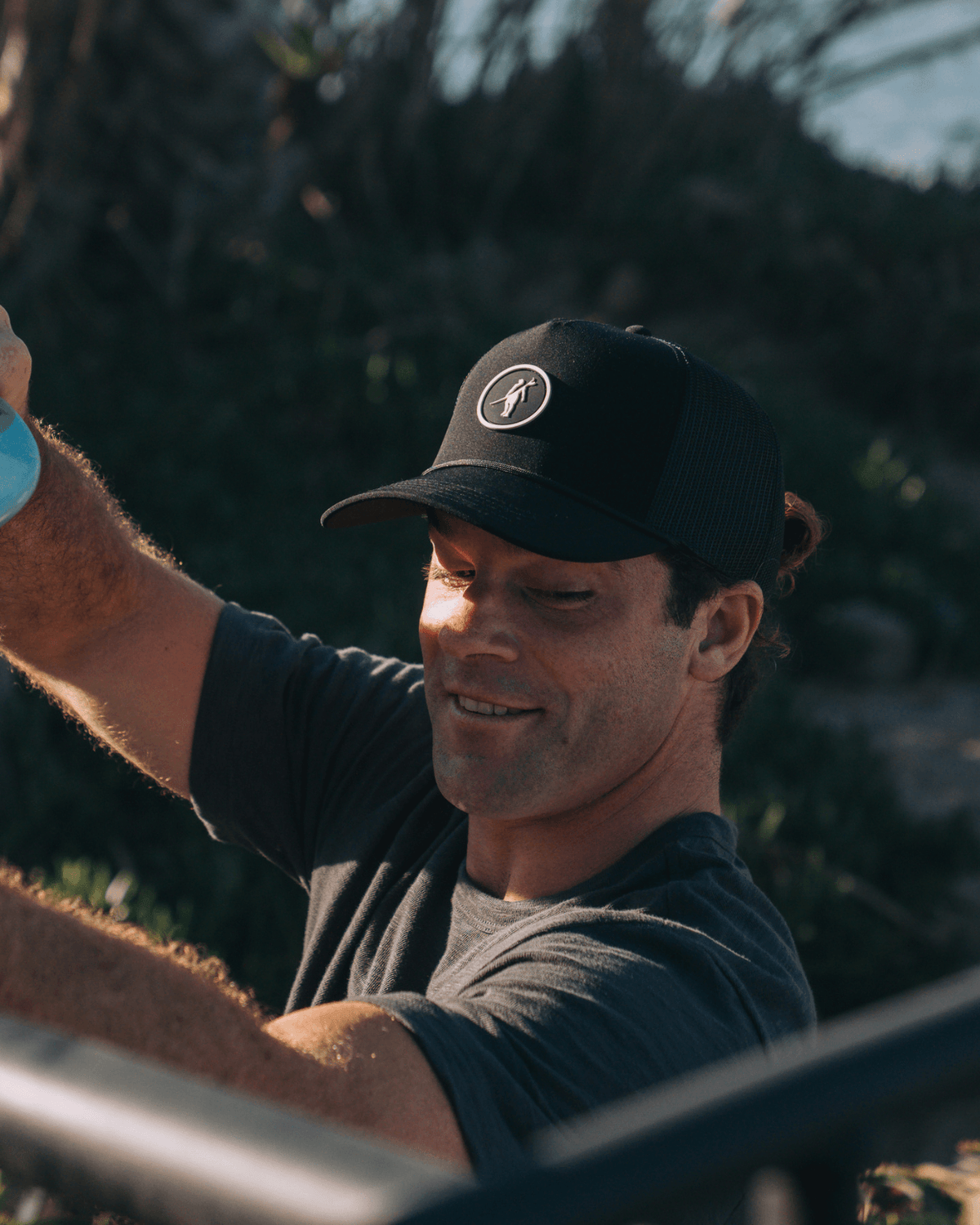 Man wearing a black cap with a logo, outdoors with greenery in the background
#color_black