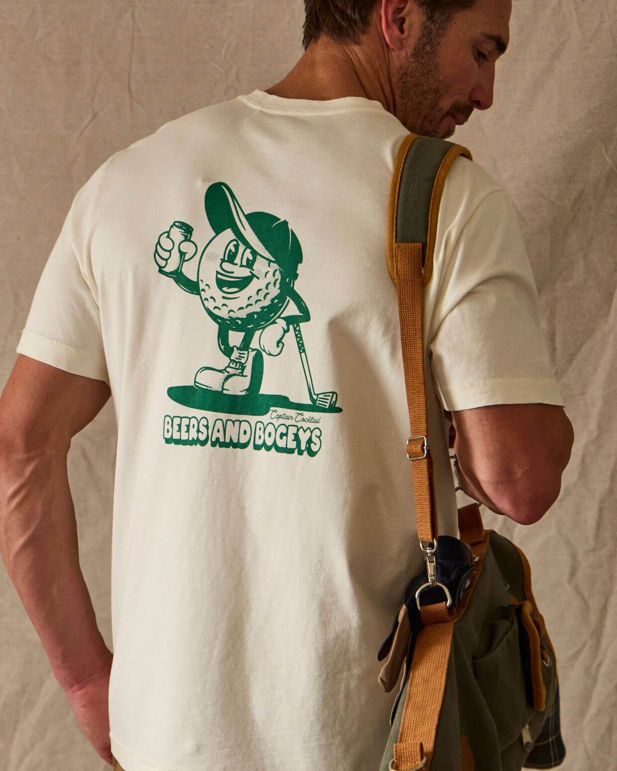 Man wearing a white t-shirt with a green graphic and text, holding a bag. #color_natural tee