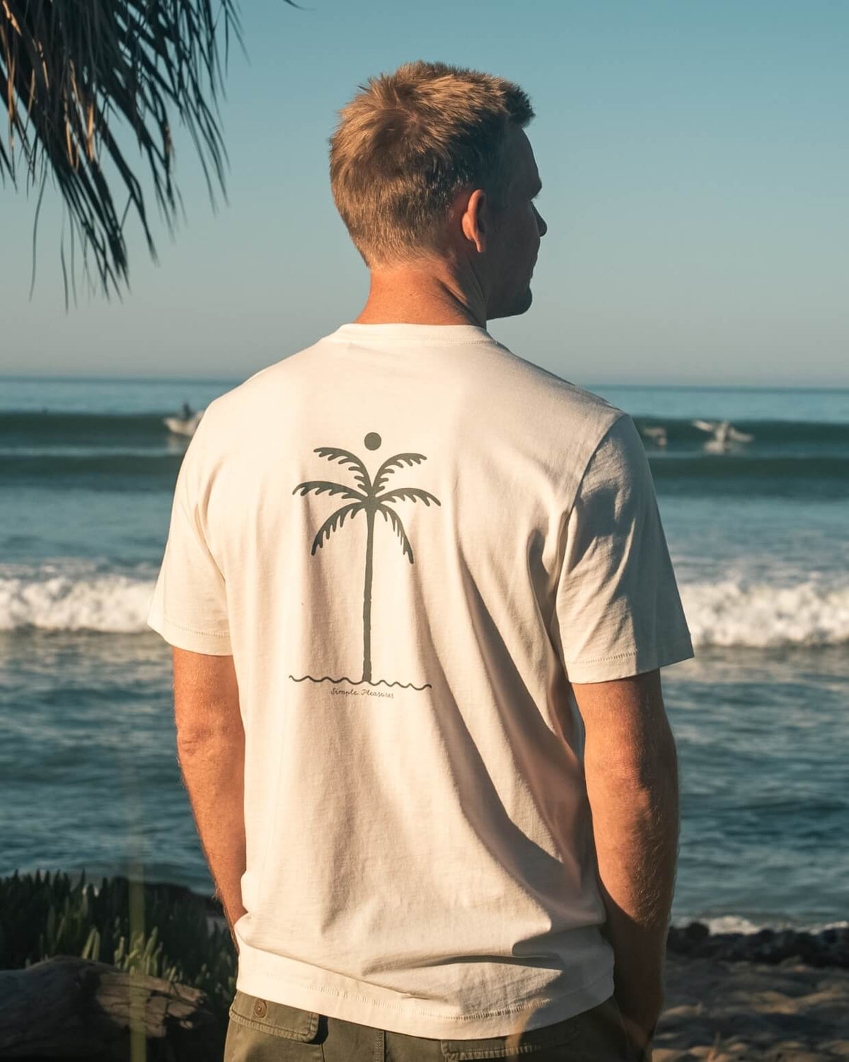 Man wearing a white t-shirt with a palm tree design on the beach #color_natural palm