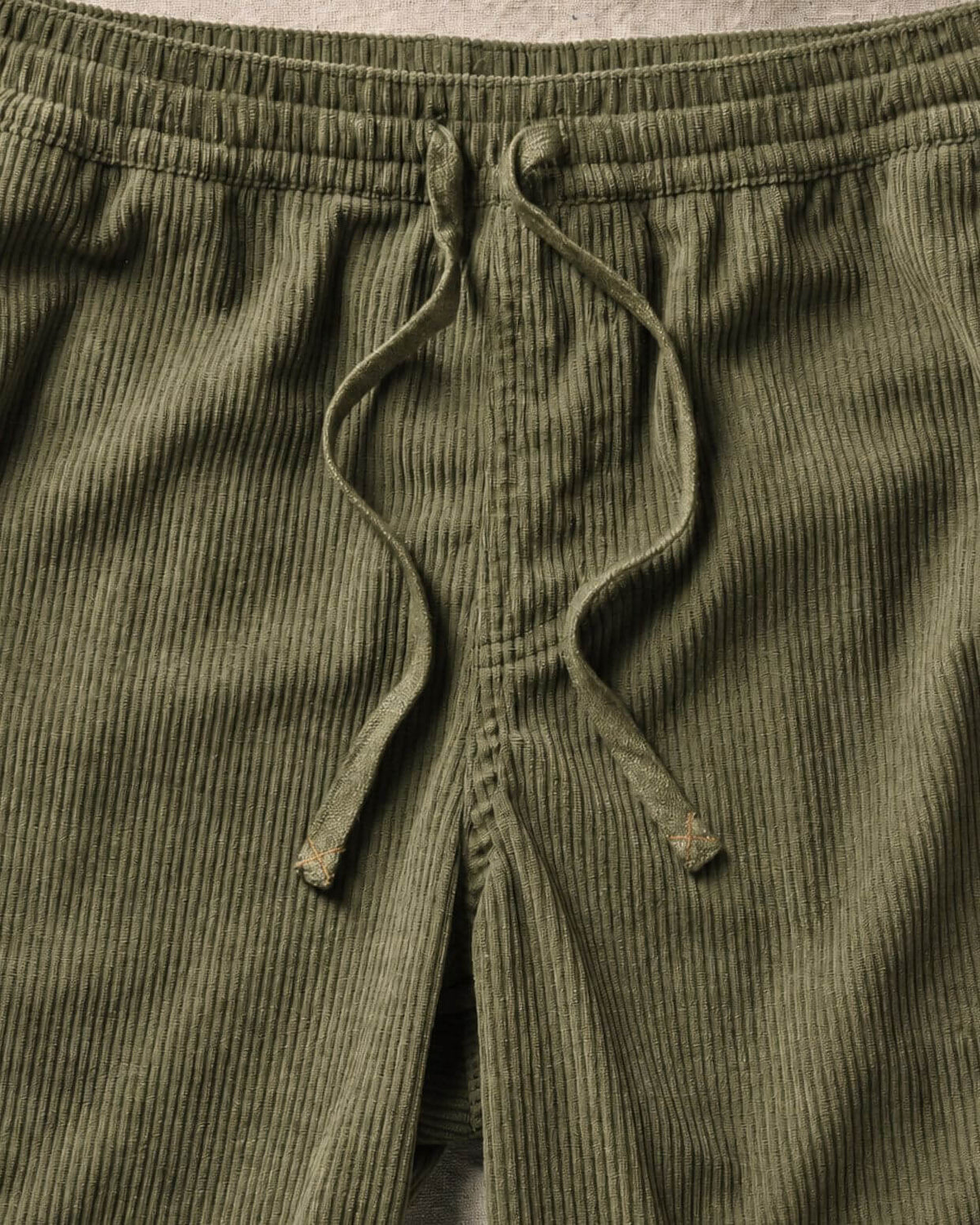 Close-up of olive green corduroy pants showing the textured fabric and drawstring waistband. #color_olive cord