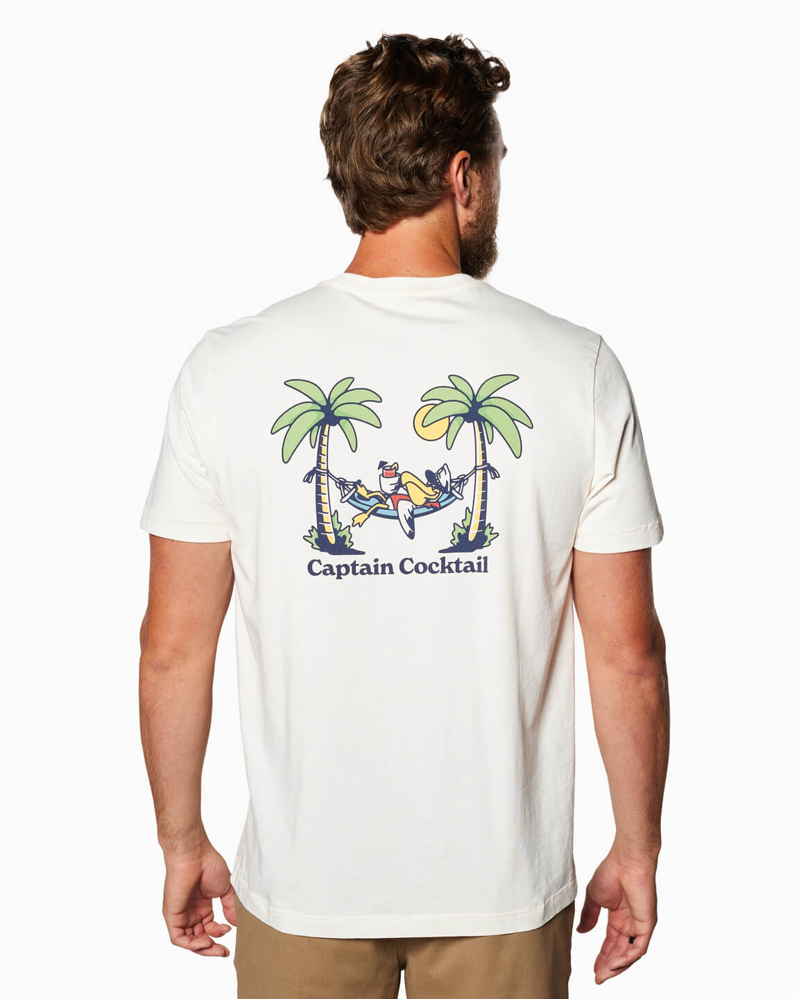 Man wearing a white Toes on the Nose Chiller Short Sleeve T-shirt with a back graphic of a relaxed character in a hammock between two palm trees and the text "Captain Cocktail.