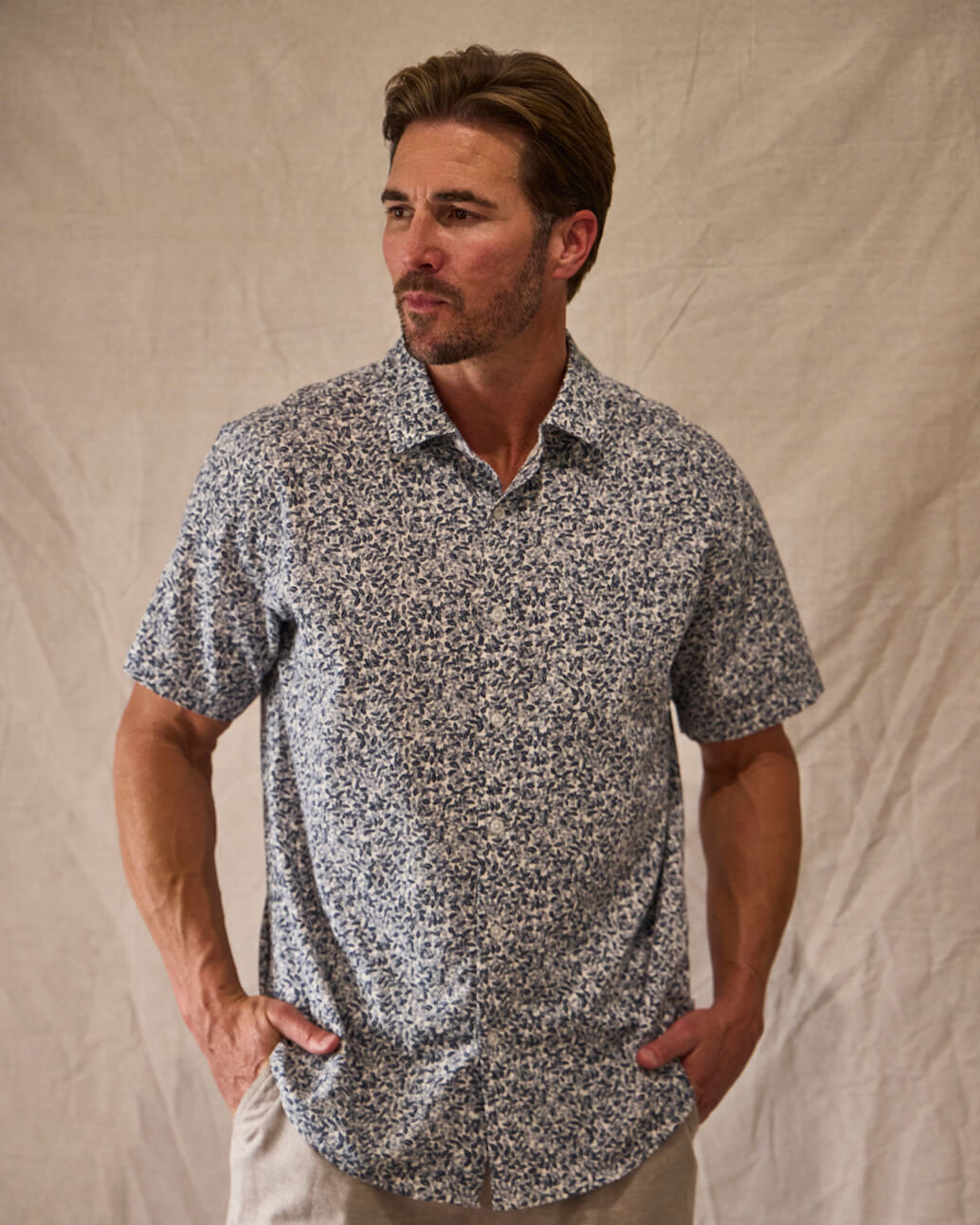 Man wearing a patterned shirt and beige pants against a plain background #color_navy leaves
