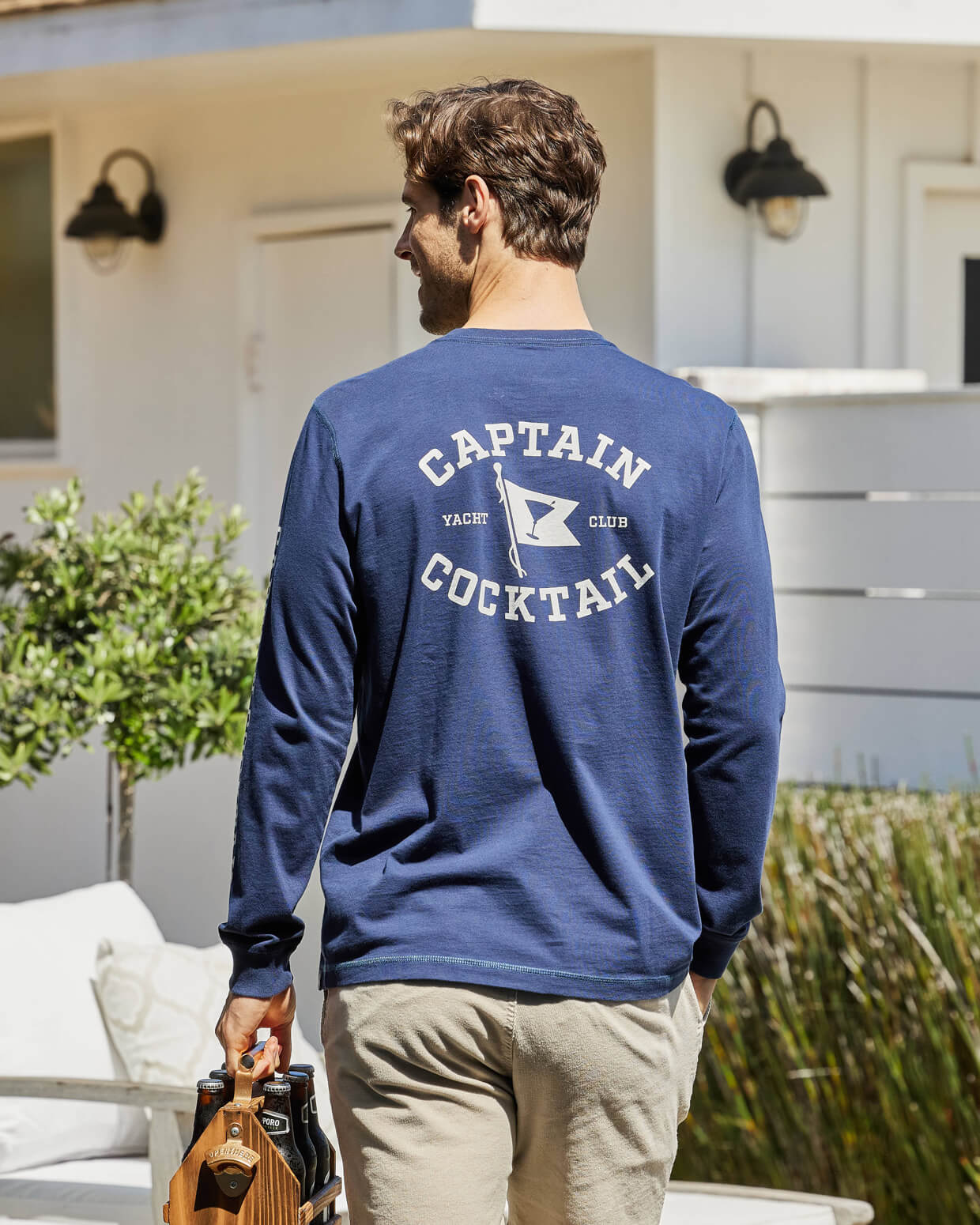 Men's navy long-sleeve T-shirt with Captain Cocktail Yacht Club graphic on the back, worn by model, outdoors.