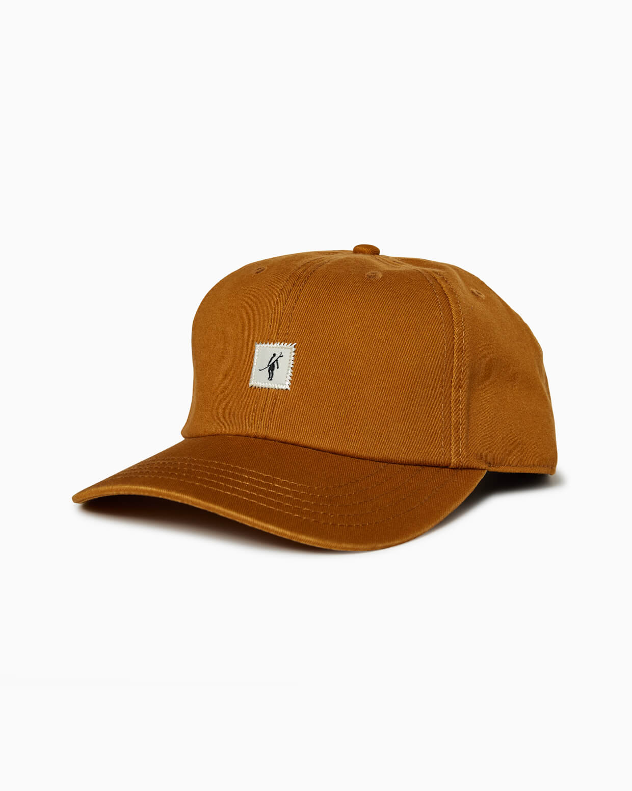 Caramel brown baseball cap with small square Toes on the Nose surfer patch, angled studio view.
