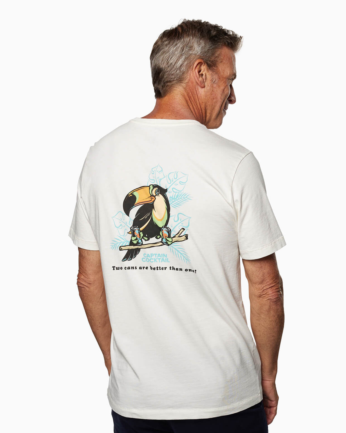 White Toes on the Nose Two Cans Short Sleeve T-shirt with a back graphic of a large toucan holding two cocktails, surrounded by tropical leaves, and the text “Captain Cocktail – Two cans are better than one!”