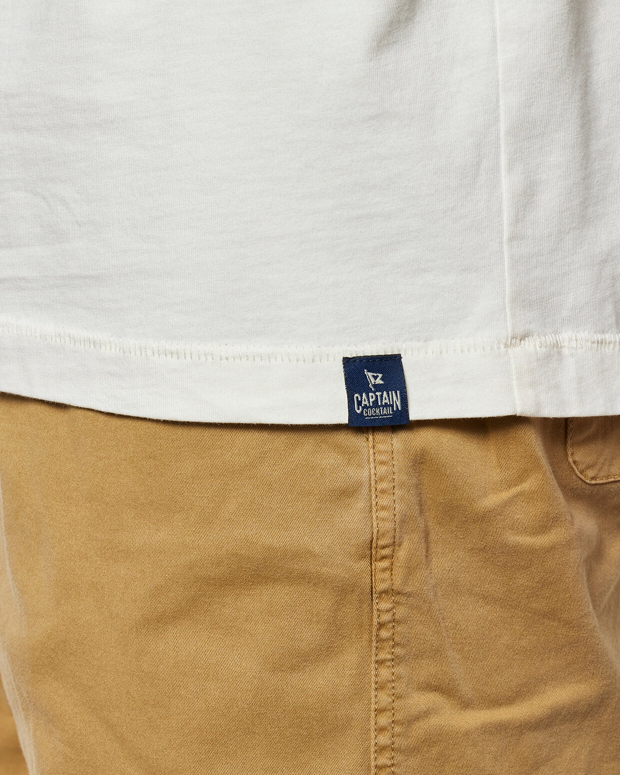 Close-up of a white shirt and tan pants with a Captain Cocktail logo tag.