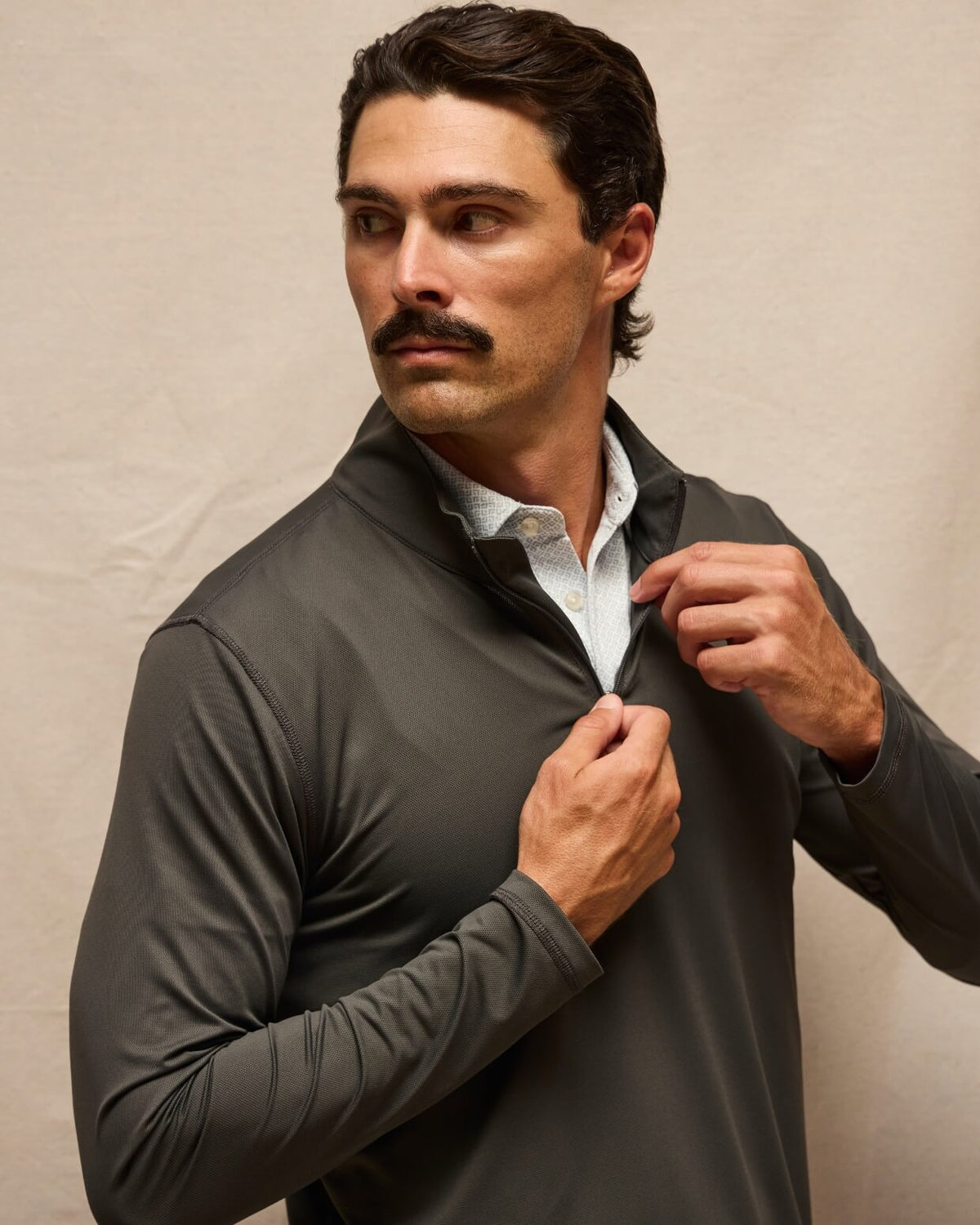 A man wearing a dark gray long-sleeve quarter-zip pullover over a white collared shirt, posing against a neutral beige backdrop. #color_black