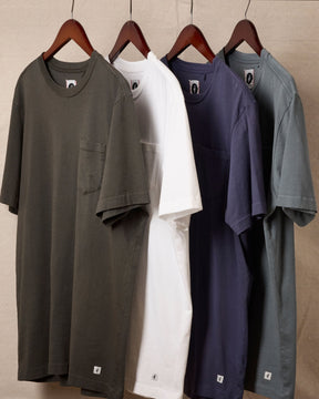 Four shirts in different colors hanging on wooden hangers against a beige wall. 