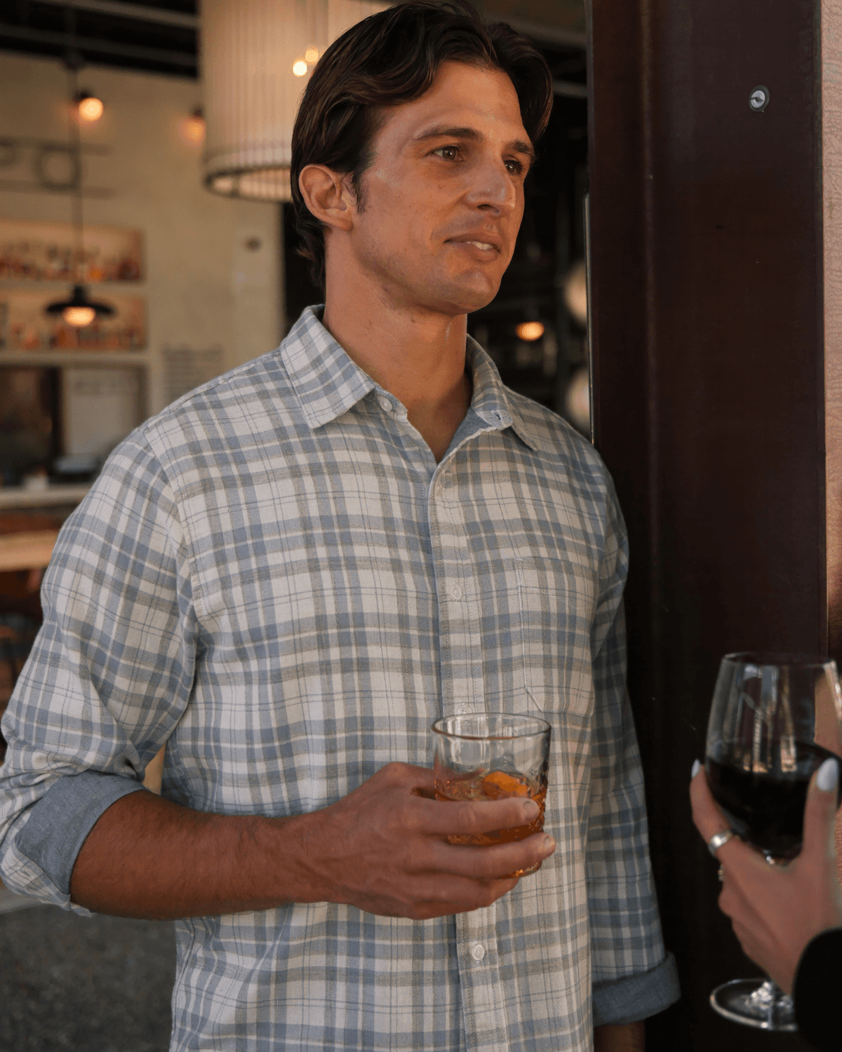 Man in a plaid shirt holding a glass of whiskey in a dimly lit bar. #color_deuce salt