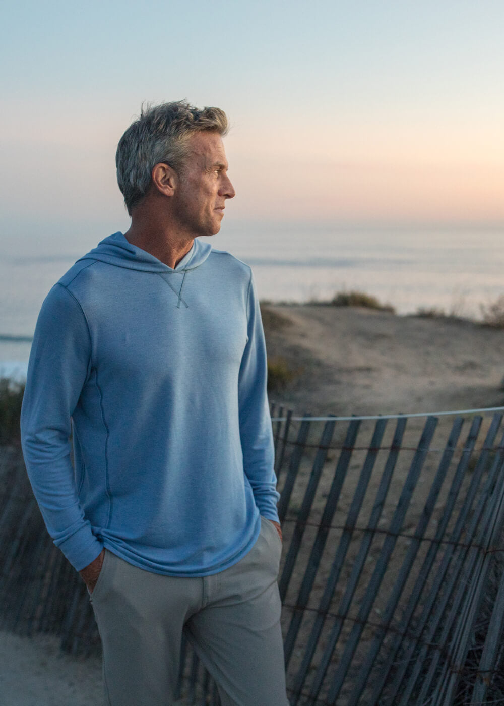 Man in a blue hoodie standing on a beach at sunset