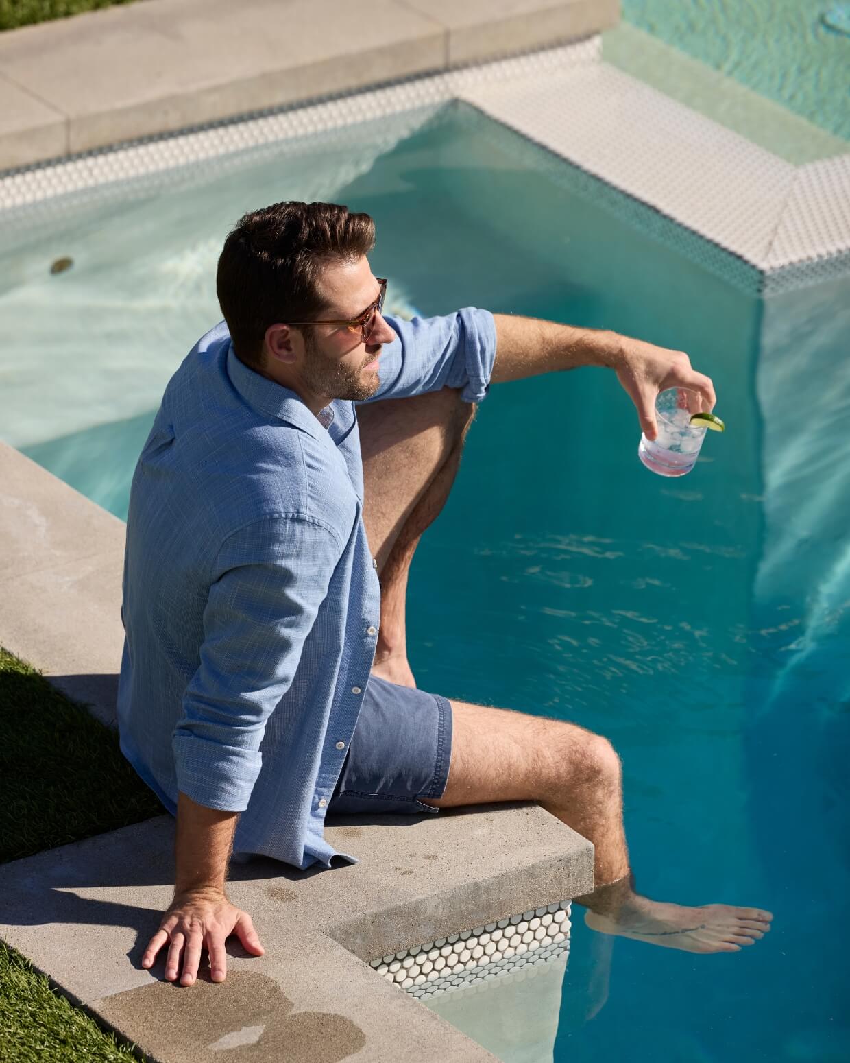 Man sitting by a pool holding a drink