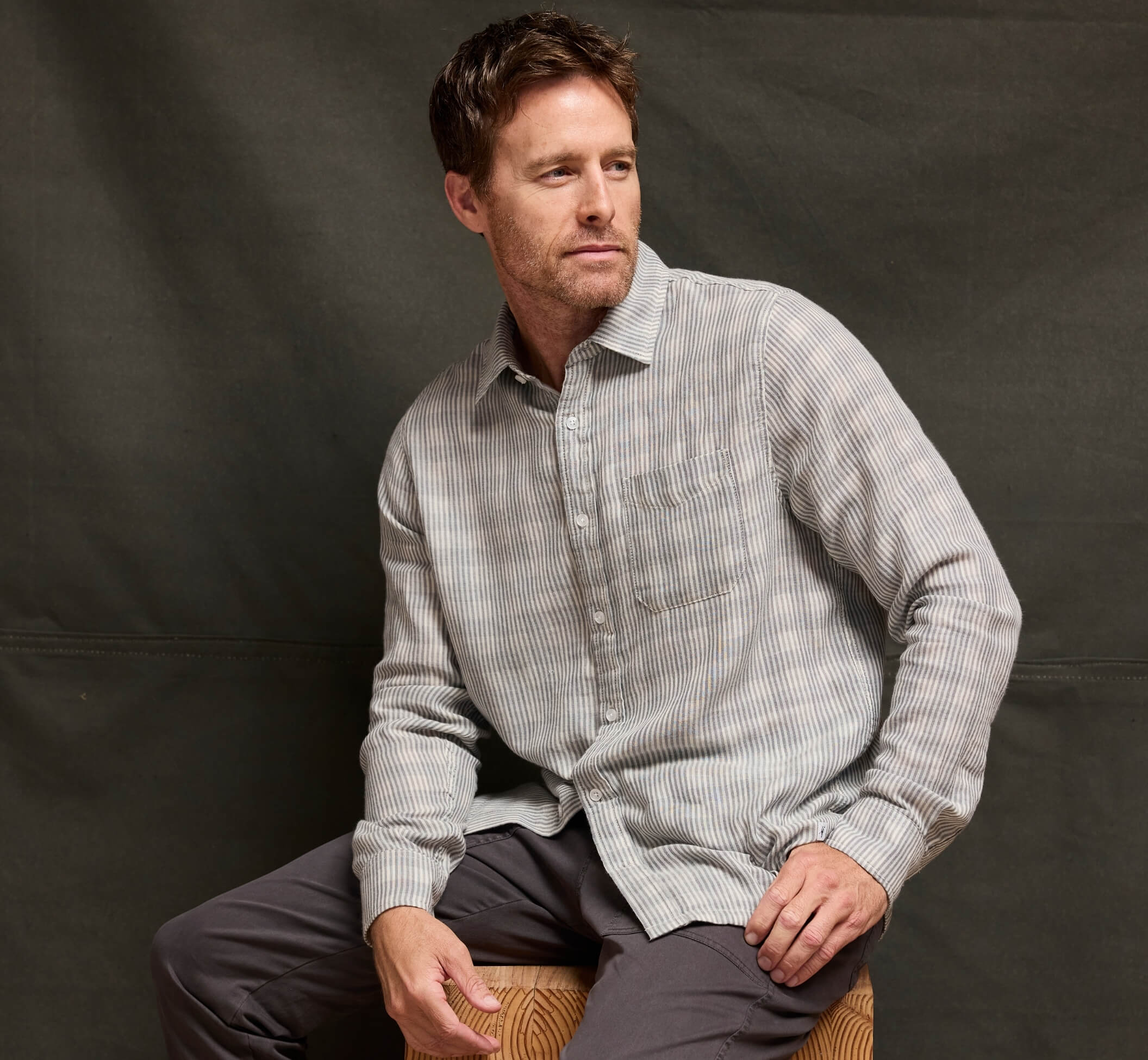 A man wearing a  charcoal gray double cloth long sleeve shirt, posing against a dark gray studio backdrop.
