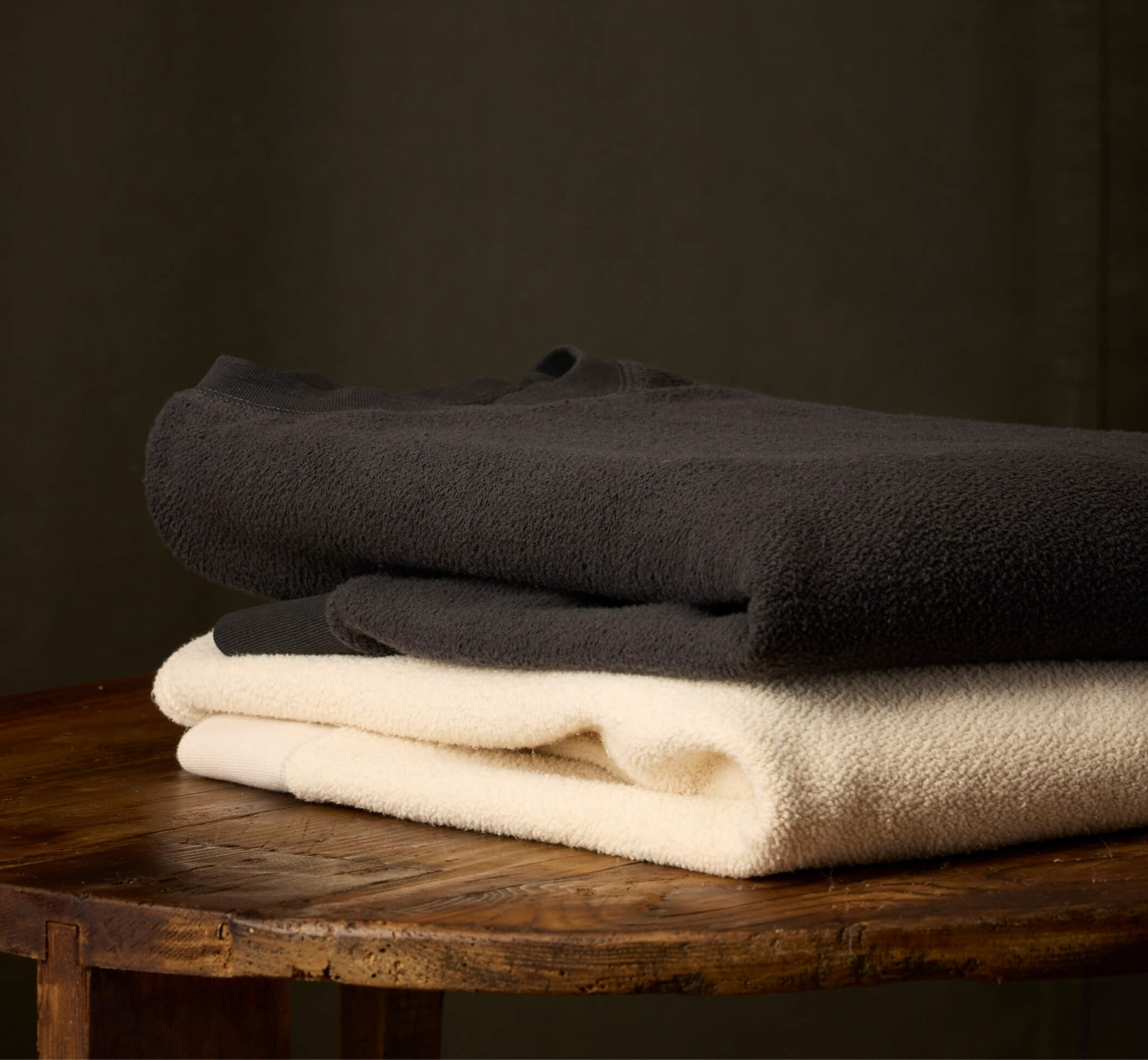 Folded crewneck on a wooden table with a dar green canvas background