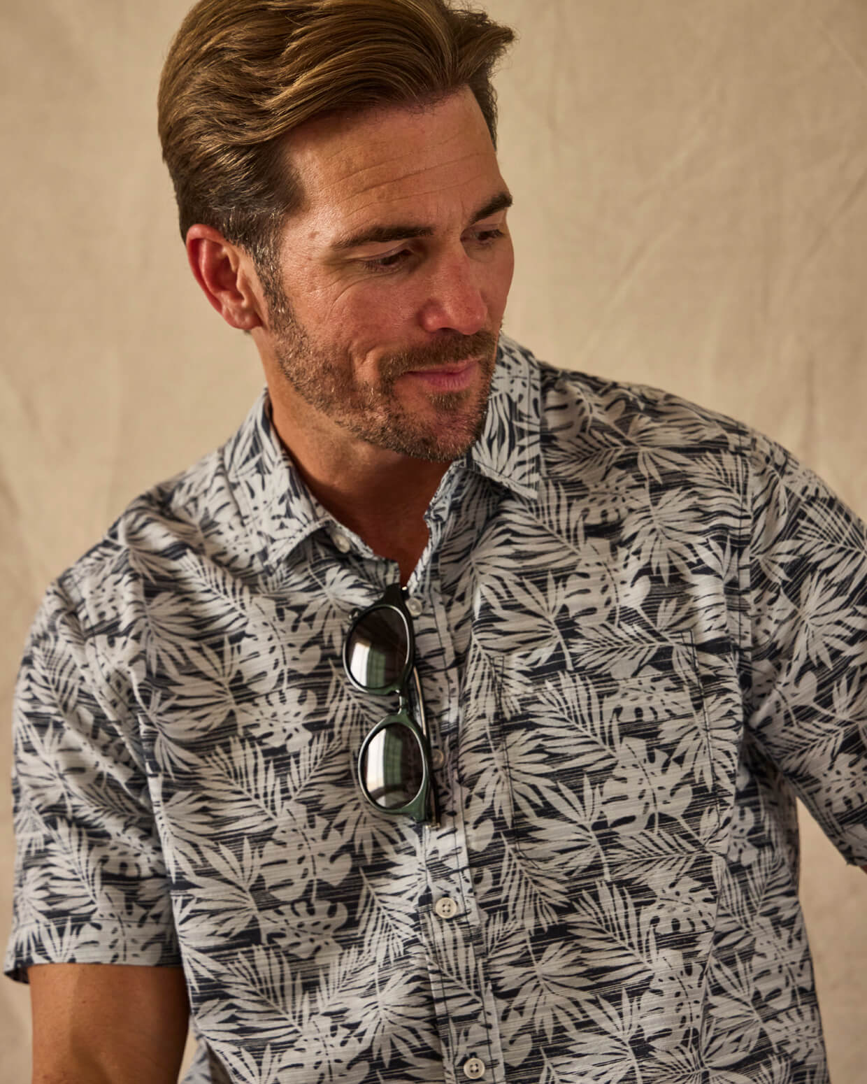 Man wearing a patterned shirt with sunglasses on a beige background