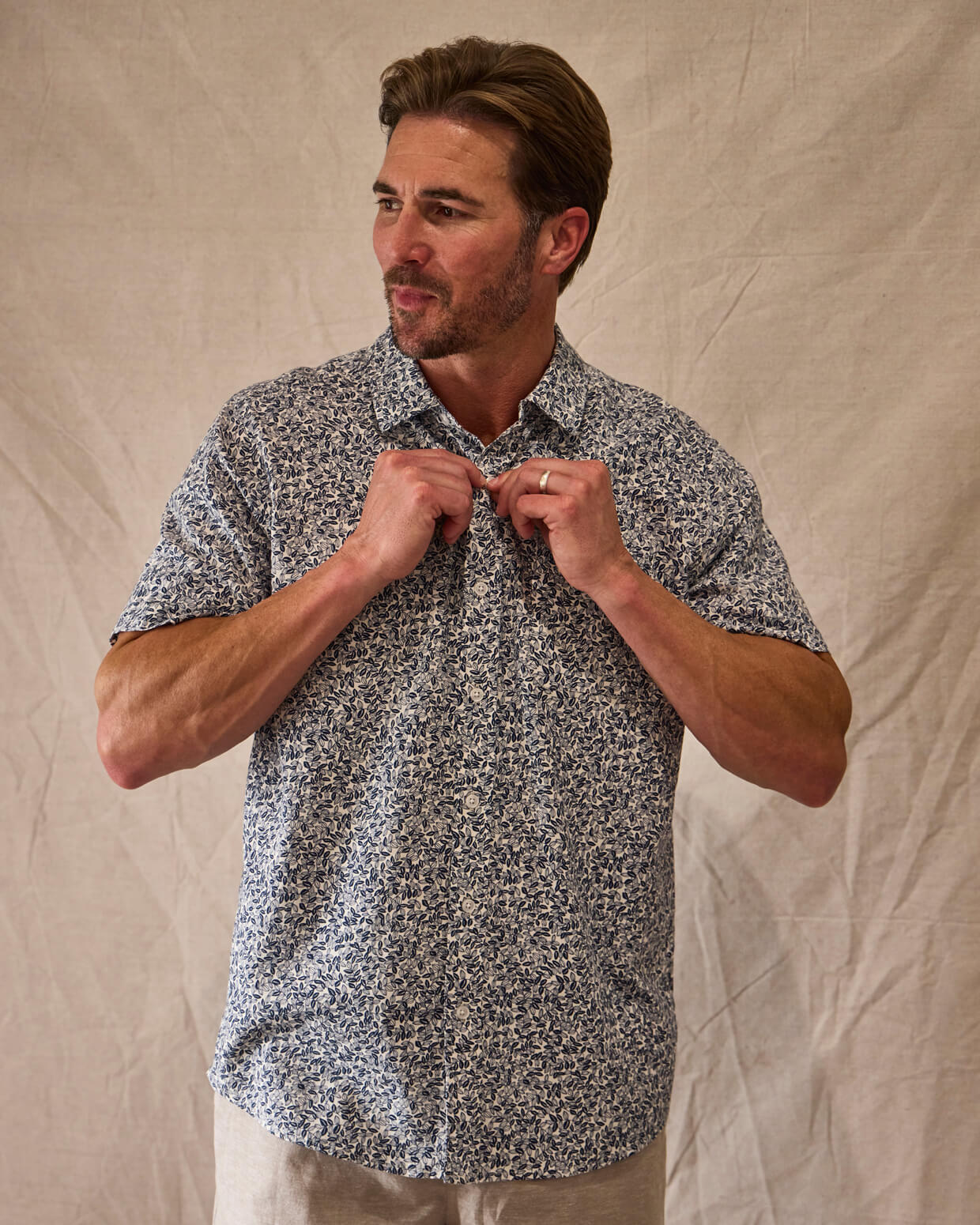 Man adjusting his floral shirt against a beige background