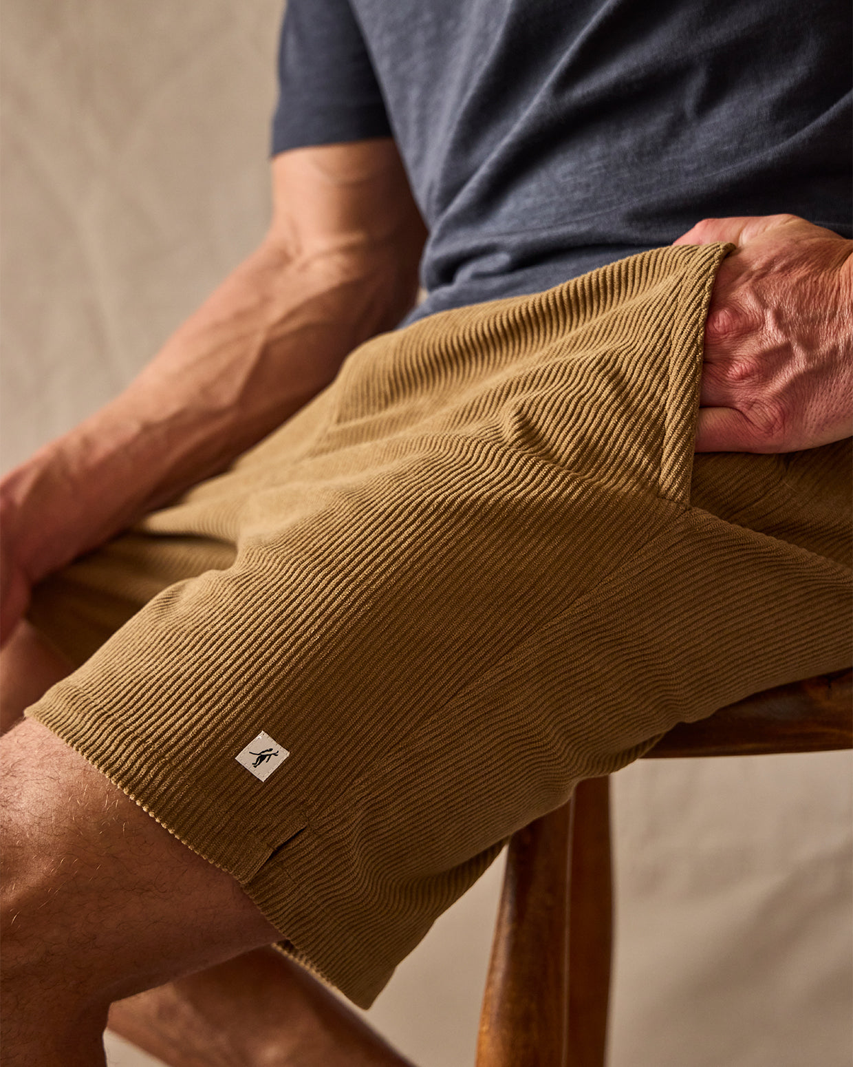 Person wearing brown corduroy shorts with a small logo, sitting on a wooden stool.