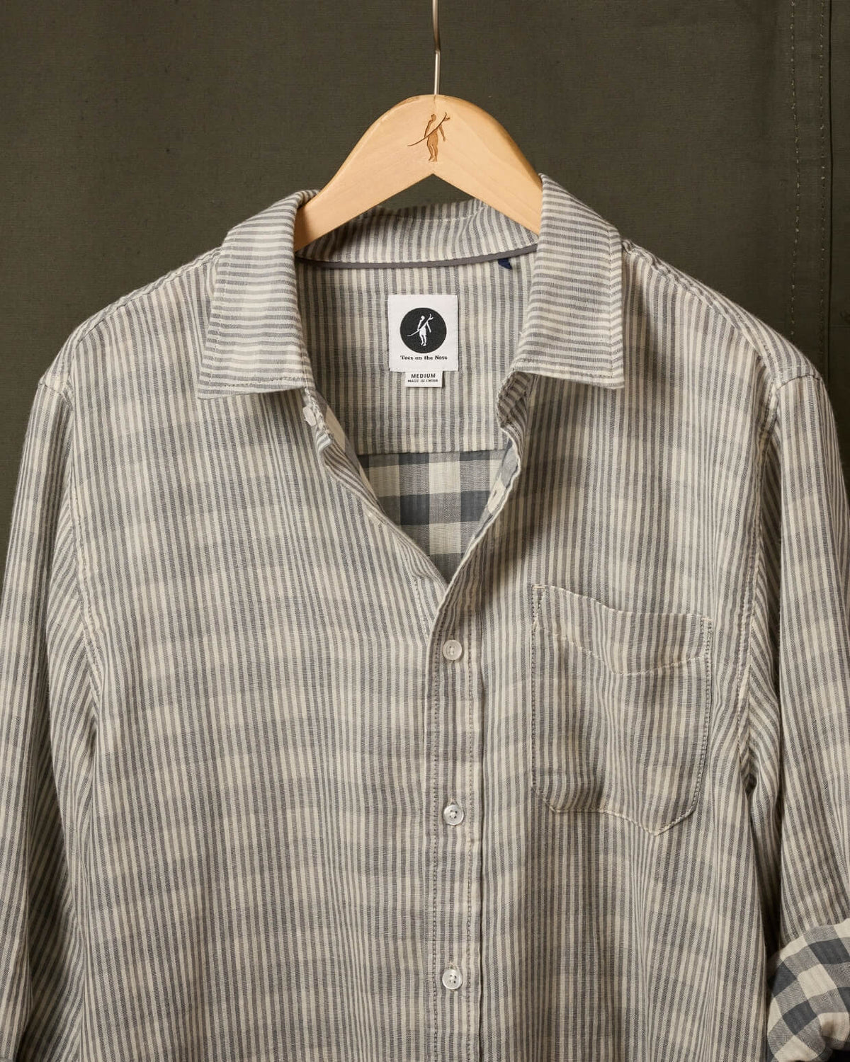 Striped shirt with a plaid lining on a hanger against a dark background #color_deuce smoke